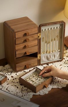 a person is holding an open wooden box with jewelry in it on a lace tablecloth