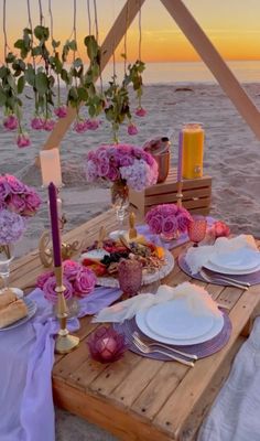 a wooden table topped with plates and flowers next to the ocean at sunset or dawn