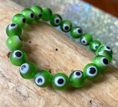 "This a simple and classy evil eye bracelet in bright grass green.  It is believed that the evil eye  protects its owner from harmful energy and negativity.  Generally worn on the left wrist if you need protection over your emotions or personal life and on the right wrist if you need protection over material things such as money.  Because the left side of our body is the one linked to our emotions as it is the side of our hearts and the right side to our brain and the analytical parts of ourselv Spiritual Green Bangle Bracelet, Green Evil Eye Round Bead Jewelry, Green Evil Eye Bead Jewelry, Green Evil Eye Round Beads Jewelry, Green Evil Eye Jewelry With Round Beads, Green Spiritual Stretch Bangle Bracelet, Green Evil Eye Bracelet With Round Beads, Green Evil Eye Bracelet With Round Beads As Gift, Adjustable Green Evil Eye Bracelet As Gift