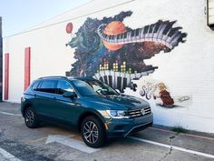 a blue volkswagen suv parked in front of a wall with an artistic mural on it