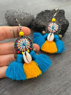 Unique fun and colorful earrings. Made with yellow and blue tassels and a beautiful round center piece made with different fabrics and strings, the earrings are adorned with beads, brass bells and shells. This pair will rock your outfit. Fun and easy to wear as they are super light. The earrings are 6cm- 2.40inch long 5.3cm- 2.10inch wide This timeless pair will brighten up your days! To see more unique and fun colorful tassel earrings, click the link below https://www.etsy.com/shop/AkashiJewelr Yellow Bohemian Earrings With Latkans, Bohemian Yellow Earrings With Latkans, Yellow Bohemian Tassel Earrings For Beach, Yellow Tassel Earrings For Festival, Handmade Blue Bohemian Tassel Earrings, Blue Bohemian Tassel Earrings For Summer, Bohemian Blue Tassel Earrings For Summer, Bohemian Blue Fringe Tassel Earrings, Bohemian Blue Handmade Tassel Earrings