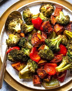 a white plate topped with broccoli and red bell peppers next to a fork