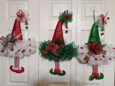 three christmas wreaths hanging on the front door with santa's stockings and hats