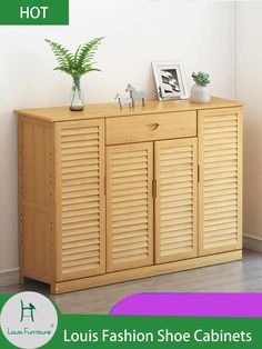 a wooden shoe cabinet with shutter doors and plants on top, in front of a white wall