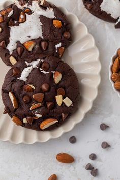 three chocolate cookies on a plate with almonds and whipped cream in the middle one is half eaten