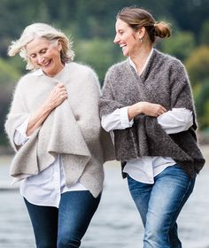 two women are walking along the water with their arms wrapped around each other and smiling