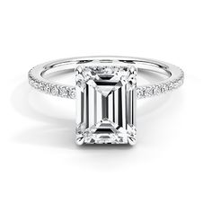 an emerald cut engagement ring with pave diamonds on the band and side stones in white gold