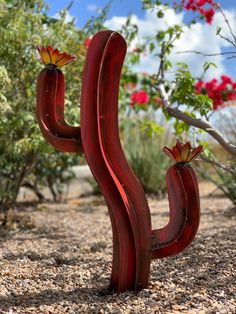 a red wooden cactus plant sitting on top of a gravel ground