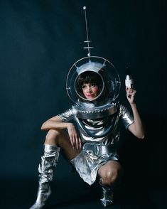 a woman dressed as an astronaut holding a remote control in one hand and a bottle in the other