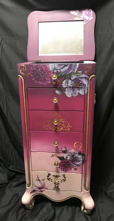 a pink and gold dresser with flowers painted on the drawers, sitting against a black background