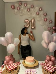 a woman standing in front of a table with balloons and cake