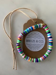 a colorful bracelet is hanging from a string on a white surface with a tag that says breeze & co