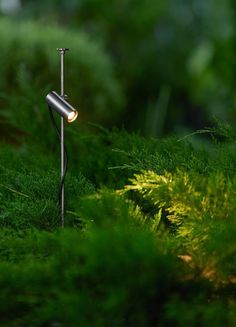 a lamp is sitting in the middle of some green grass and plants, with one light on it's side