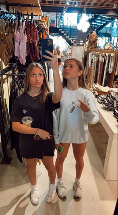 two young women are standing in a clothing store and one is holding up her cell phone