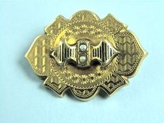 "Very pretty 18k gold pin from the mid Victorian Period c. 1870 is formed of a hollow shield-shaped body etched with a wavy pattern, tiny star bursts and decorative trim.  The top has a stylized ribbon surmounted that is decorated with taille d'Epergne enameling and is set with two grey seed pearls.  This is a fine example of the etching that was typical of the period.  The back has a C-clasp and tube hinge and also has a hole that likely held a hook or loop to have it serve as a pendant.  Measu Victorian Gold Engraved Brooches, Victorian Engraved Medallion Brooches, Victorian Engraved Gold Brooches, Ornate Engraved Yellow Gold Brooches, Ornate Gold Engraved Brooches, Victorian Gold Brooch With Screw Back, Wavy Pattern, Gold Pin, Tiny Star