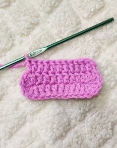 a pink crocheted case sitting on top of a white blanket next to a pair of knitting needles