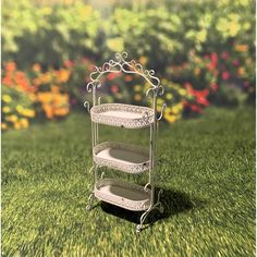 a three tiered shelf sitting on top of a lush green grass covered field with flowers in the background