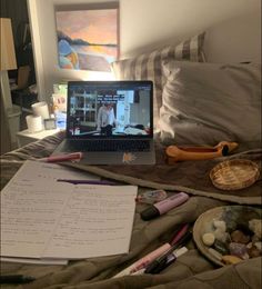 an open laptop computer sitting on top of a bed next to papers and other items