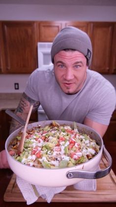 a man is holding a large casserole dish with many toppings on it