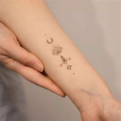 a woman's arm with a small flower and crescent tattoo on the left wrist