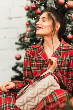 a woman sitting in front of a christmas tree with her handbag on her hip