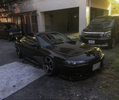 a black car is parked in front of a building with two other cars behind it