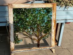 an old mirror with a tree in it on the ground next to a blue bench