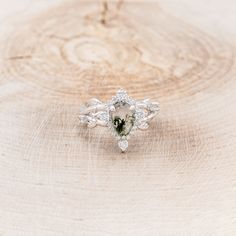 an engagement ring with a pear shaped green stone surrounded by small white diamonds on a wooden surface