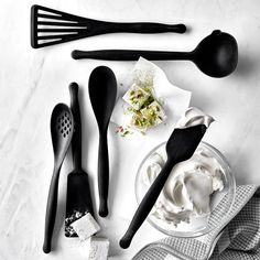 black kitchen utensils are laid out on a white counter top, including whipped cream and spoons