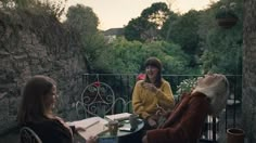 three women sitting at an outdoor table talking to each other while one woman holds a flower in her hand