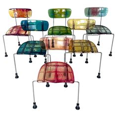 six different colored chairs sitting next to each other on metal legs with wheels in front of them