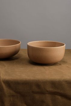 two bowls sitting on top of a brown tablecloth covered table next to each other