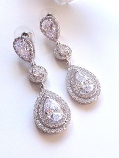 This earring features a white gold plated clear white teardrop cubic zirconia surrounded by 2 layers of little cubic zirconia gems (about 60 gems around it),  dangle from a white gold plated halo round cubic zirconia and a LARGE pear shaped cubic zirconia post earrings. Size: 5.3 (L) x 1.8  (W) cm or 2.1(L)  x 0.72  (W) inches long. Matching Bracelet and Necklace: https://www.etsy.com/listing/225770378/bridal-bracelet-double-halo-round-rose Note: The pear shaped post stud earring used in this design is sightly larger than my other design which has the similar post earrings. If it is a larger pear shaped post stud used, I will mentioned it as large in the listing and the title. **NOTE: CUBIC ZIRCONIA HAS MANY DIFFERENT GRADES, AND ALL THE CUBIC ZIRCONIA USED IN MY DESIGN IS OF THE HIGHEST Q Diamond Teardrop Chandelier Earrings, Dazzling White Teardrop Crystal Earrings, Dazzling Diamond White Teardrop Chandelier Earrings, Dazzling Diamond White Teardrop Crystal Earrings, Dazzling Teardrop Crystal Earrings In Diamond White, Teardrop Chandelier Earrings With Diamond Accents, White Cubic Zirconia Teardrop Earrings For Party, Cubic Zirconia Drop Chandelier Earrings, Diamond White Teardrop Bridal Earrings