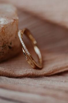 two gold wedding bands sitting on top of a pink cloth next to a stone slab