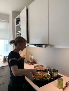 a woman cooking food on top of a stove next to a pan filled with vegetables