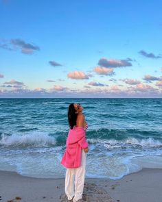 a woman standing on top of a sandy beach next to the ocean under a blue cloudy sky