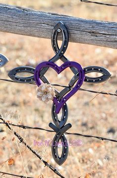 a purple heart shaped key hanging from a barbed wire fence with flowers in the center