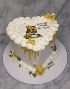 a white heart shaped cake with yellow icing and winnie the pooh on it