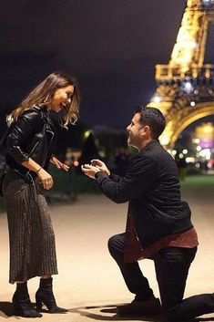 a man kneeling down next to a woman in front of the eiffel tower