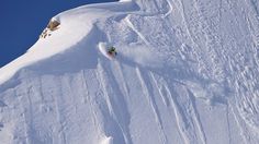 a person is skiing down a steep snowy mountain with blue skies in the back ground