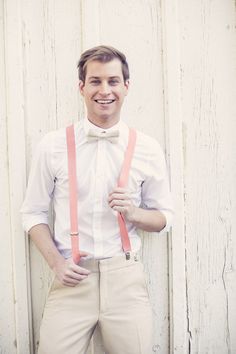 a man wearing suspenders and a bow tie poses for a photo in front of a white wall