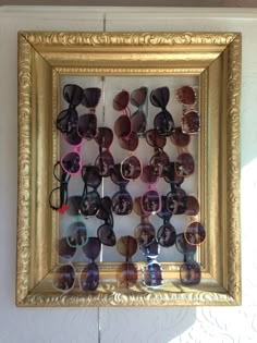 there are many pairs of sunglasses on display in the gold framed frame that is hanging on the wall