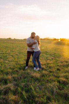 a man and woman hugging in the middle of a grassy field with sun behind them