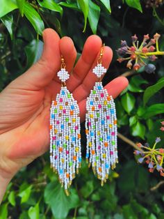 a person is holding up some colorful beaded earrings in front of green leaves and flowers