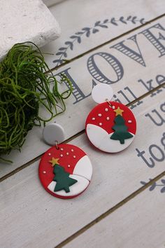 two red and white christmas themed earrings sitting on top of a wooden table next to a potted plant