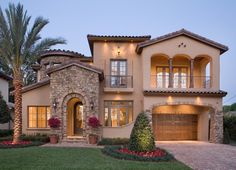 a large house with two garages and palm trees in the front yard at dusk