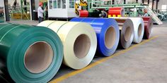 rolls of colored steel in a factory with workers working behind them on the other side