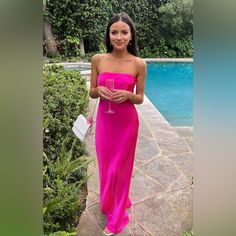 a woman in a pink dress standing next to a pool holding a glass of wine