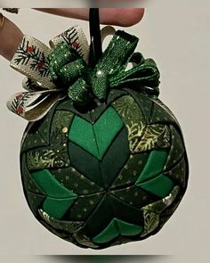 a hand holding an ornament with green leaves and bows on it's side