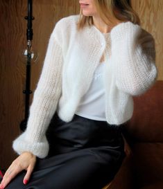 a woman sitting in a chair wearing a white sweater and black skirt with her hands on her hips